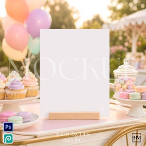 May include: A vertical rectangular white sign mockup standing on a light wooden base. The sign is positioned on a table with cupcakes on a white stand, a glass jar filled with pastel candies, and colorful balloons in the background. The sign measures 8x10 inches.