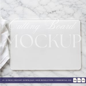 May include: A rectangular white cutting board mockup with rounded corners, featuring the text Cutting Board MOCKUP overlaid in the center. A white fabric cloth is visible on the left side. The dimensions are 15 x 11 inches.