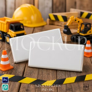 May include: Two rectangular white objects with silver edges are displayed on a wooden surface, alongside toy construction vehicles, a yellow hard hat, and traffic cones. The objects measure 5.25 x 5.5 inches. A black and yellow caution tape is in the foreground.