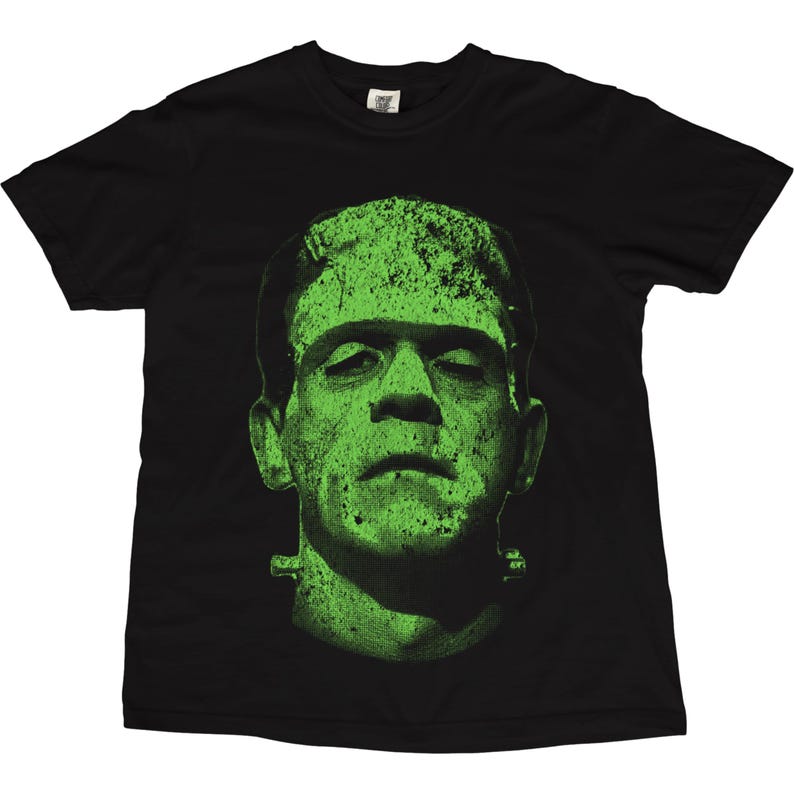 May include: Black t-shirt featuring a green graphic of Frankenstein's monster. The monster's face is prominently displayed, with a textured, distressed effect. The design is centered on the shirt, creating a bold and eye-catching look. A classic horror movie theme.