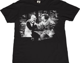以下が含まれることがあります： 黒いTシャツ。白黒画像で、ガスマスク姿とピエロ姿の2人の人物が公園のベンチに座っている。画像はグレースケール写真で、人物同士が交流している様子が写っている。