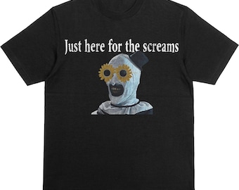 以下が含まれることがあります： 「Just here for the screams」の白い文字が入った黒いTシャツ。ひまわりの目と小さな黒い帽子をかぶったピエロのような人物のグラフィックが特徴です。その人物は白い顔とフリルカラーをしています。