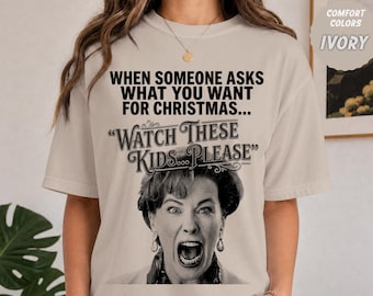 以下が含まれることがあります： アイボリー色のTシャツ。黒い文字で「WHEN SOMEONE ASKS WHAT YOU WANT FOR CHRISTMAS... "WATCH THESE KIDS... PLEASE"」と書かれており、その下に口を大きく開けた表情の女性の白黒写真プリントが施されています。