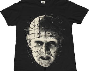 May include: Black t-shirt featuring a detailed, grayscale graphic of a character's face with nails embedded in the head. The character has a pale complexion and a grimacing expression. The shirt is a classic crew neck.