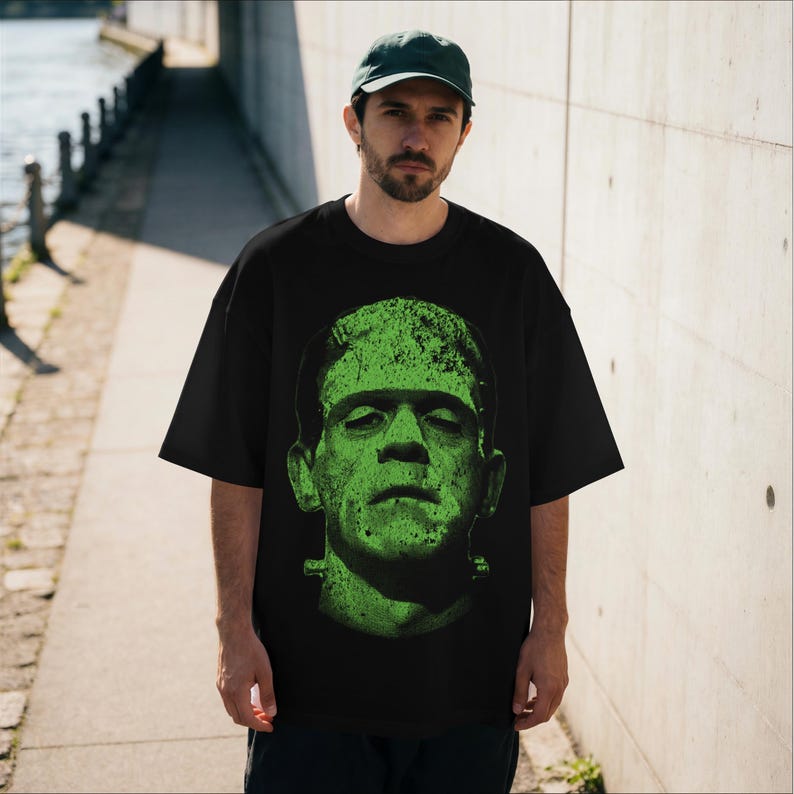 May include: Black t-shirt featuring a distressed green graphic of Frankenstein's monster. The oversized tee has short sleeves and a crew neck. The graphic is a close-up of the monster's face, with visible stitches and bolts.