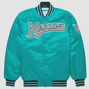 May include: Teal satin jacket with the word "Marlins" across the chest in white and gray lettering. The jacket has a black, white, and teal striped collar, cuffs, and hem. A team logo patch is on the right sleeve.