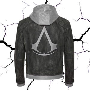 Pode incluir: Casaco de couro cinza escuro com capuz cinza. A parte de trás do casaco apresenta um grande emblema prateado. O casaco tem um aspeto desgastado com costuras visíveis e uma faixa cinza na parte inferior e nos punhos.