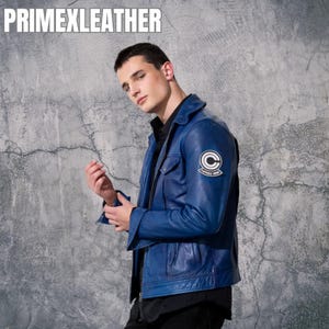 Puede incluir: Chaqueta de cuero azul con una camisa negra debajo. La chaqueta tiene un parche en la manga con un círculo blanco y el texto "CAPSULE CORP". El texto "PRIMEXLEATHER" está en la parte superior de la imagen.
