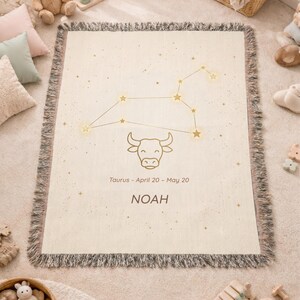 Könnte beinhalten: Beige Decke mit Fransen. Die Decke zeigt ein goldenes Stier-Sternbild-Design, eine Stier-Illustration und den Namen "NOAH". Der Text lautet "Stier - 20. April - 20. Mai".