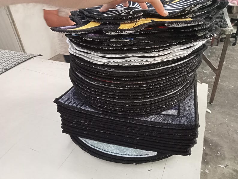 Pode incluir: Uma pilha de tapetes decorativos pretos e redondos com costuras brancas nas bordas. Os tapetes t&ecirc;m um desenho na superf&iacute;cie superior com detalhes em amarelo e branco. Os tapetes est&atilde;o empilhados uns sobre os outros.