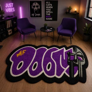 Peut inclure: Un tapis de forme personnalisée présentant le texte MF DOOM en lettres graffiti violettes audacieuses avec un contour blanc sur fond noir. Le côté droit du tapis affiche un graphique de masque gris et noir intégré au design.