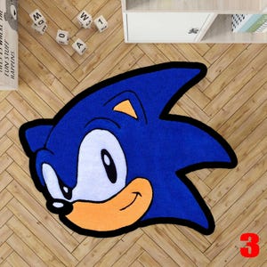 May include: A blue rug shaped like Sonic the Hedgehog's head, with a white face, orange accents, and a black outline. The rug is on a wooden floor. A red number 3 is in the bottom right corner.