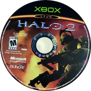 May include: Halo 2 Xbox Live game disc. The disc features the game title in blue and a futuristic soldier holding a weapon. The disc has a black background with orange and red hues. The Xbox Live and Microsoft Game Studios logos are also visible.
