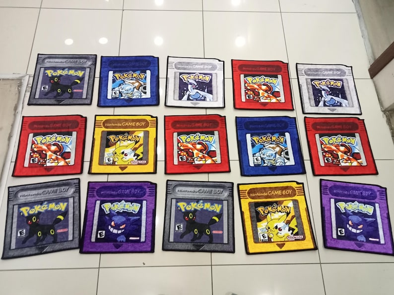 Pode incluir: Uma cole&ccedil;&atilde;o de tapetes retangulares coloridos, projetados para se assemelharem aos cartuchos Pok&eacute;mon do Nintendo Game Boy vintage. Cada tapete apresenta um personagem Pok&eacute;mon diferente e o logotipo "Pok&eacute;mon", com o texto "Nintendo Game Boy".