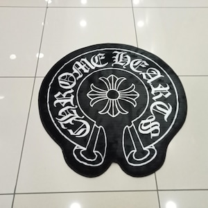 Pode incluir: Tapete preto e branco com o texto "CHROME HEARTS" em fonte g&oacute;tica. O tapete apresenta um design de cruz central e uma forma de ferradura. O tapete est&aacute; sobre um ch&atilde;o ladrilhado.