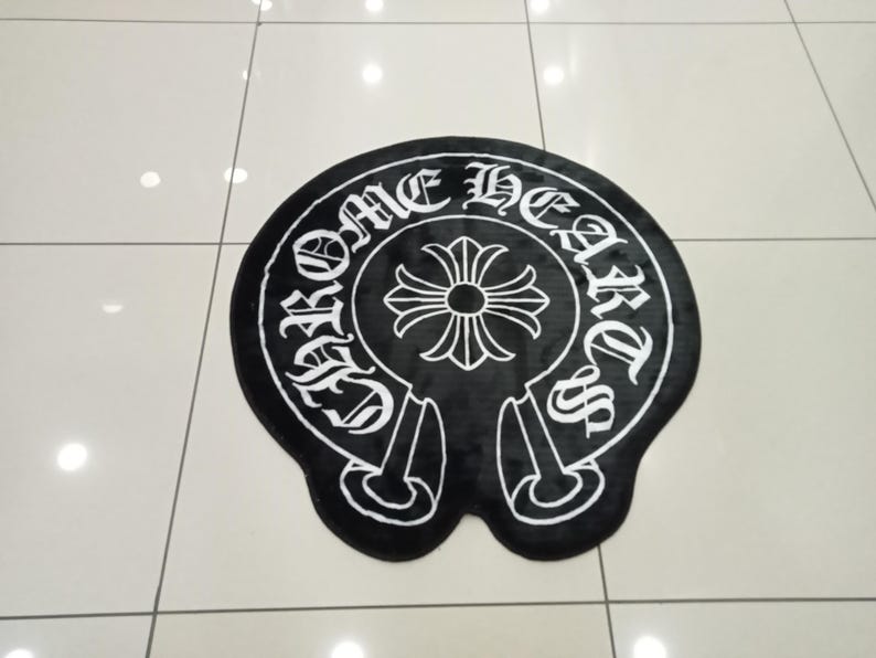 Pode incluir: Tapete preto e branco com o texto "CHROME HEARTS" em fonte g&oacute;tica. O tapete apresenta um design de cruz central e uma forma de ferradura. O tapete est&aacute; sobre um ch&atilde;o ladrilhado.
