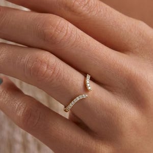 Op de afbeelding: Een goudkleurige open ring met kleine, heldere edelstenen. De ring buigt om de vinger, met de edelstenen langs de buitenranden. De ring wordt gedragen op een hand met lichtgroene nagellak.