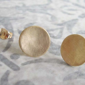 May include: A pair of gold-toned round disc earrings. The earrings are smooth and have a brushed finish.