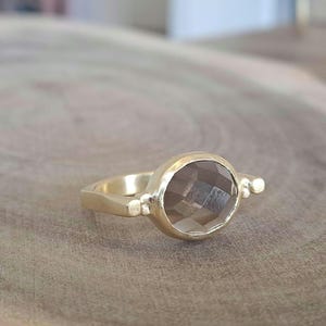 May include: A gold ring featuring a faceted smoky quartz gemstone. The ring has a plain band and a bezel setting.