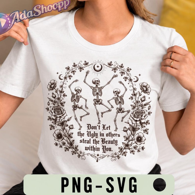 May include: A white t-shirt featuring a black graphic of three dancing skeletons encircled by a floral wreath of roses and vines. The text "Don't Let the Ugly in others steal the Beauty within You" is printed in the center in a gothic-style font.