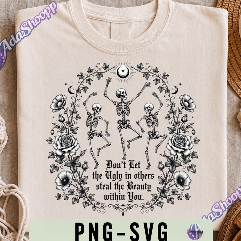 May include: A cream-colored t-shirt featuring a black graphic of three dancing skeletons surrounded by a floral wreath of roses and ivy. Above the skeletons is a crescent moon and star. The text reads, Don't Let the Ugly in others steal the Beauty within You.