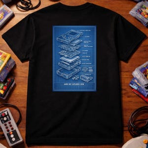 May include: Black t-shirt with a blue blueprint design showing an exploded view of a Game Boy. The image is surrounded by retro gaming consoles, controllers, and game cartridges on a wooden surface.