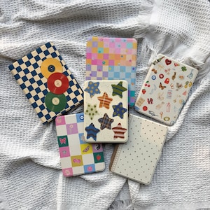 May include: Six rectangular notebooks with varied covers: one with blue and cream checkers and vinyl records, one with a pastel checkered star pattern, one with colorful star illustrations, one with assorted icons, one with pastel squares and motifs, and one with polka dots.