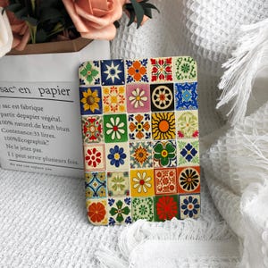 May include: A square coaster with a vibrant, patterned tile design. The design incorporates floral and geometric patterns in blue, yellow, orange, green, and red. The coaster is displayed on a white surface.