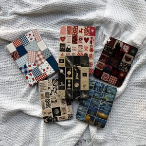May include: Five rectangular e-reader cases featuring collage-style designs. One has a blue and red patchwork pattern, one has red and white icons, one has black and red gothic motifs, one has beige celestial imagery, and one has blue starry night art.