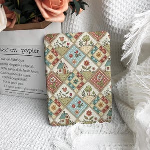 May include: A rectangular e-reader cover featuring a repeating diamond pattern with illustrations of small houses, flowers, trees, and birds in muted shades of red, blue, green, and yellow on a cream background with a subtle grid texture.