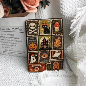 May include: A rectangular card featuring a grid of twelve postage stamp-style illustrations with Halloween themes, including a skull, a black cat in a witch hat, a mushroom, a pumpkin, a haunted house, a ghost, an eye, and the text Happy Halloween.