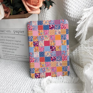 May include: A rectangular e-reader cover featuring a vibrant patchwork design composed of small squares in various floral, polka dot, and striped patterns. The color palette includes shades of pink, blue, yellow, and red, creating a dense, multi-colored grid across the entire surface of the protective case.
