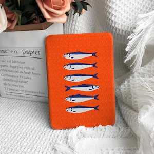 May include: A rectangular orange e-reader case featuring a repeating vertical pattern of six stylized blue and white fish. The case has a textured surface and rounded corners, displaying a consistent graphic design across the front cover.