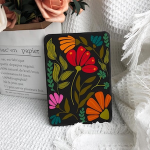 May include: A black rectangular e-reader cover featuring a vibrant floral pattern with red, orange, pink, and teal petals, accented by olive green leaves and stems. The design covers the entire front surface with stylized botanical illustrations.