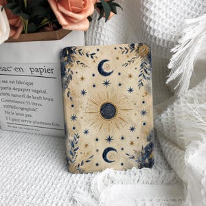 Può includere: Una targa decorativa rettangolare con sfondo color crema caratterizzata da un motivo centrale a sole blu scuro circondato da raggi dorati. Il design include lune crescenti blu scuro, varie forme di stelle e accenti botanici a foglia blu.