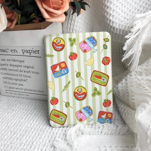 Peut inclure: Une coque de tablette rectangulaire avec un motif à rayures verticales vert clair et blanc, ornée d'illustrations de boîtes de sardines, de tomates rouges, d'olives vertes, de quartiers de citron et de brins d'herbes fraîches dispersés.