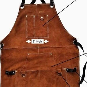 May include: A brown leather apron featuring black adjustable shoulder straps with a cross-back design, multiple storage pockets, and metal rivets. A central pocket is labeled with a 7 inch width indicator. The apron includes black webbing straps.