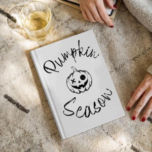 Peut inclure: Un livre à couverture rigide blanc avec le texte noir Pumpkin Season et un dessin central de citrouille d'Halloween avec un œil en forme de bouton et un autre en forme de croix. Le motif est imprimé dans une police manuscrite sur fond blanc.