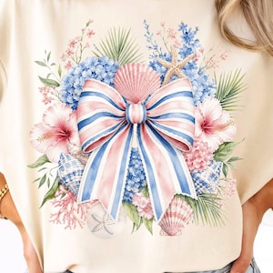Peut inclure: Un t-shirt couleur crème arborant un motif central composé d'un grand nœud rayé dans des tons rose, blanc et bleu. Le nœud est entouré d'une composition aquarelle de fleurs d'hibiscus roses, d'hortensias bleus, de coquillages et d'étoiles de mer.