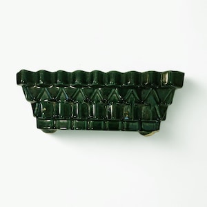 May include: A dark green ceramic planter with a rectangular shape and a textured, geometric pattern. The planter has a scalloped top edge and sits on small feet. The glossy finish enhances the rich color and intricate design.