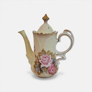 May include: Cream-colored porcelain coffee pot with a gold-colored finial and handle accents. The pot features a floral design with pink roses and green leaves. The spout and handle are curved.