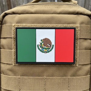 May include: A rectangular patch featuring the Mexican flag, with green, white, and red vertical stripes. The white stripe includes the Mexican coat of arms. The patch is affixed to a tan fabric background, likely a tactical bag or gear.