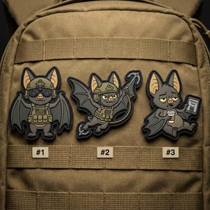 May include: Three tactical patches featuring cartoon bats in military gear. The patches are numbered #1, #2, and #3. The bats are in various poses, including one holding a coffee cup and another with a grappling hook.