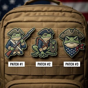 May include: Three embroidered patches featuring cartoon frogs in patriotic attire. Patch #1 depicts a frog holding a rifle, Patch #2 shows a frog with a rope, and Patch #3 has a frog wearing a bandana. The patches are on a tan backpack.