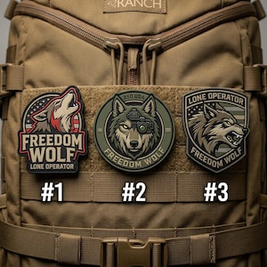 May include: Three embroidered patches with wolf designs are displayed on a tan backpack. The patches feature the text "FREEDOM WOLF" and "LONE OPERATOR". One patch has a howling wolf, another has a wolf with a camera, and the third has a snarling wolf.