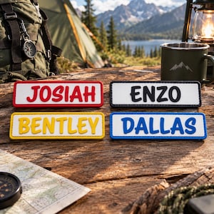 May include: Four rectangular name patches with raised lettering. The top left patch is white with red text reading JOSIAH. The top right is white with black text reading ENZO. The bottom left is white with yellow text reading BENTLEY. The bottom right is white with blue text reading DALLAS.