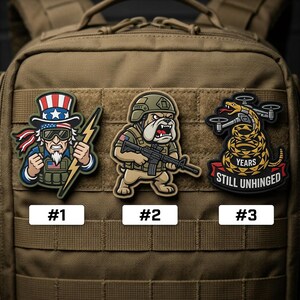 May include: Three embroidered patches with military-themed designs. One features Uncle Sam with a lightning bolt, another a bulldog soldier with a rifle, and the third a snake with a drone. Each patch is numbered and set against a tan backpack.