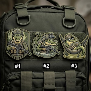 May include: Three green and tan embroidered patches featuring cartoon alligators in military gear. One alligator is in a hammock, another is in water, and the third is standing. Each patch has a number below it.