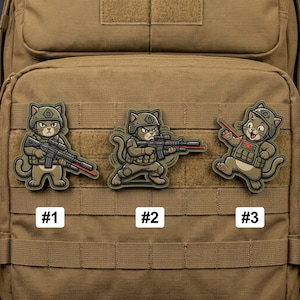 May include: Three tactical patches featuring cartoon cats in military gear. Each patch depicts a cat with a helmet and combat vest, holding a rifle. The patches are numbered #1, #2, and #3, and are in shades of green, brown, and tan.