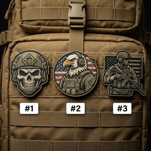 May include: Three military-themed patches are displayed on a tan backpack. The patches include a skull in a helmet, an eagle with headphones and an American flag, and a soldier holding a rifle. Each patch has a number label.